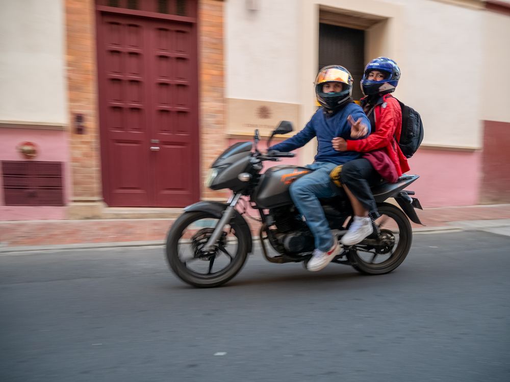 Two riders on a motorbike passing through a city street.